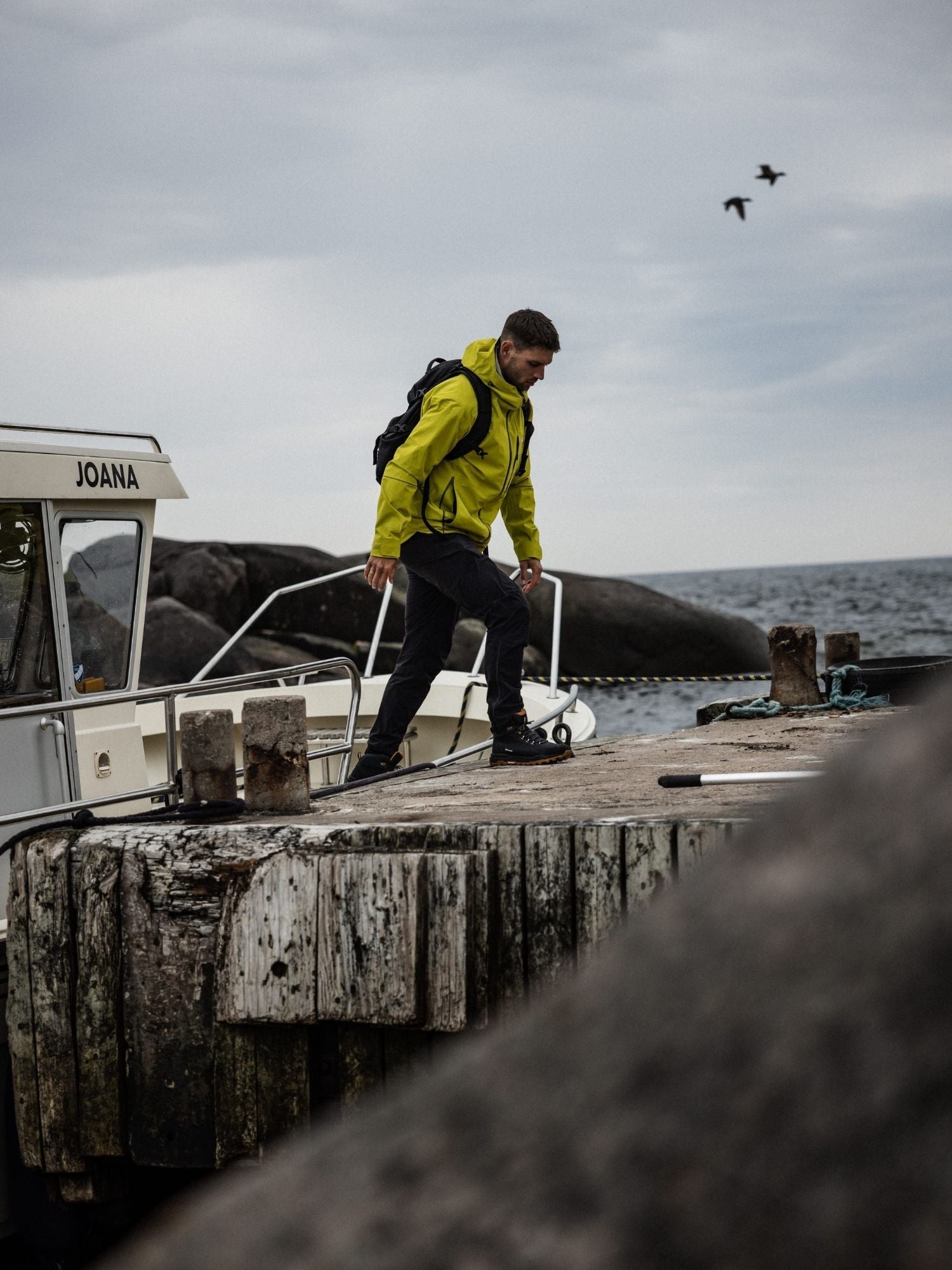 En person i rödbruna vandringskängor och svarta byxor trampar på en stor, strukturerad sten utomhus. Fotot är taget från en låg vinkel med fokus på kängan och stenen.