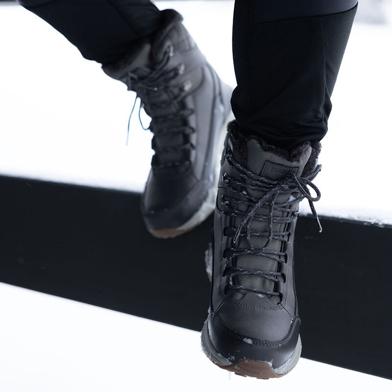 Närbild på en person som bär Halti Dundee Mid DX Vinterskor Dam, stående på snöig svart mark.