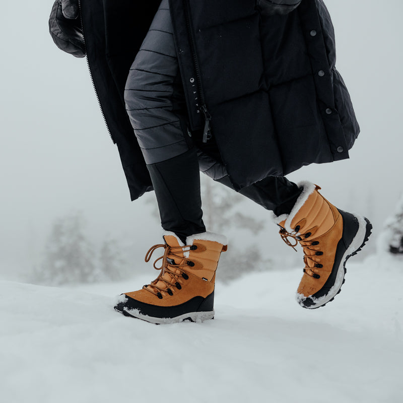 En person i Halti Tornio DrymaxX Vinterskor går genom snö en dimmig dag med träd i bakgrunden.
