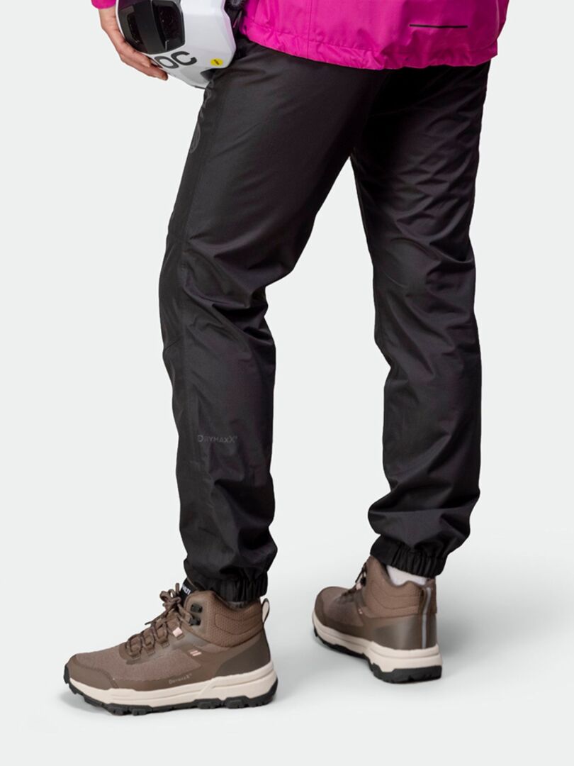 En person i svarta byxor, rosa jacka och Halti Fara 3 DX Mid Outdoorskor Dam håller i en vit hjälm, sedd bakifrån.