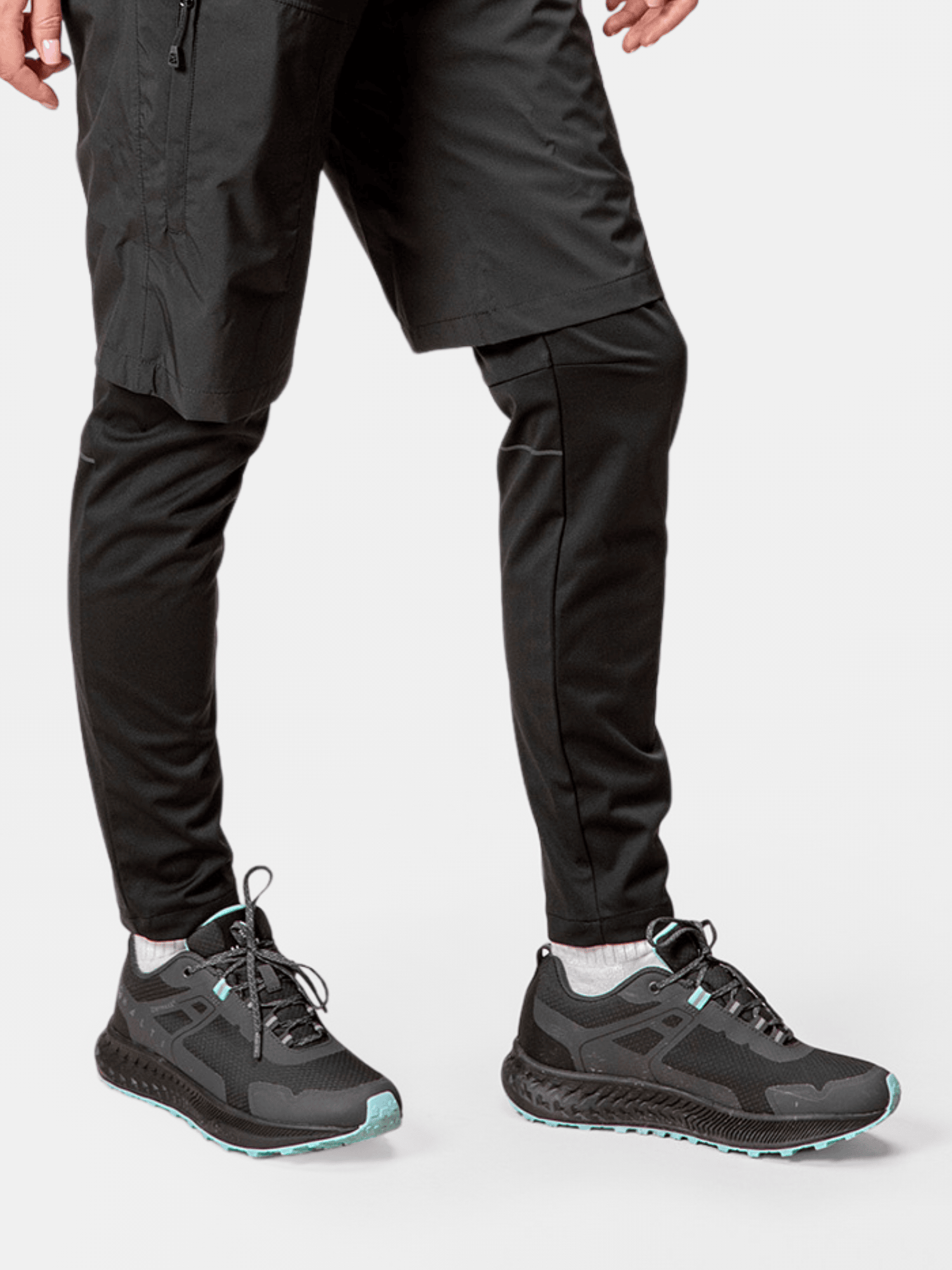 Person som bär Halti Pallas Low 2 DrymaxX Hybrid Sneaker Dam, svarta joggingbyxor och shorts mot en vit bakgrund.