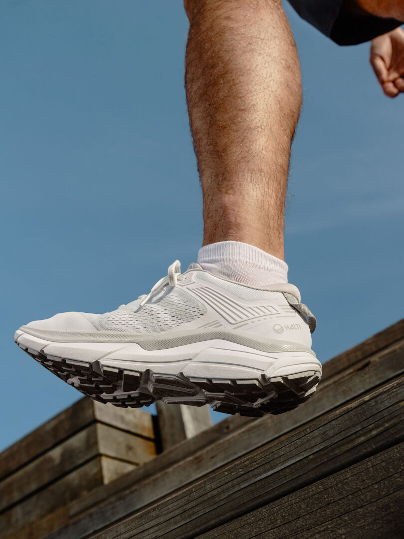 En person i Halti Tempo 3 Sneaker Herr går på en träyta utomhus under en blå himmel.