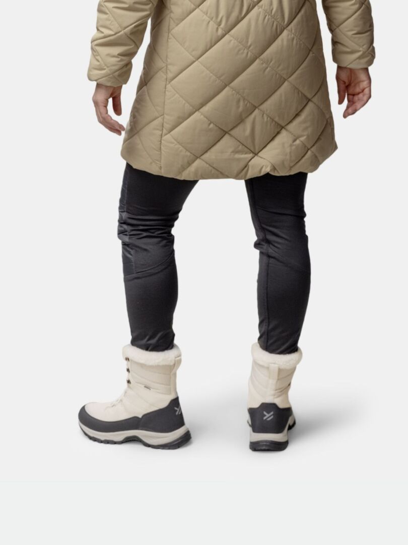 Person klädd i brun quiltad rock, svarta byxor och Halti Tornio 2 DX Vinterskor, sedd bakifrån.