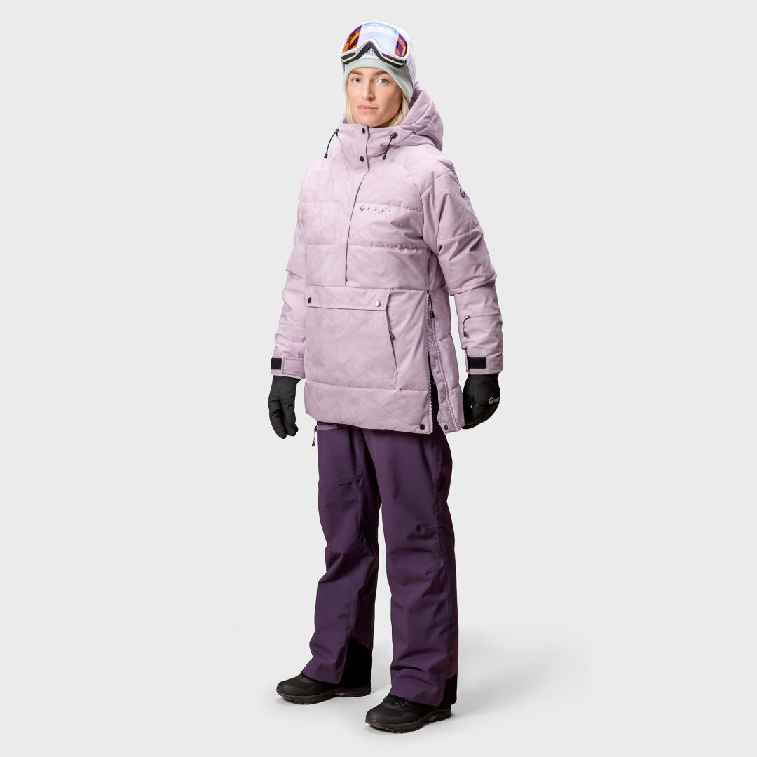 Person som bär ljuslila Halti Chowper Skidanorak Dam, mörklila snöbyxor, handskar, skyddsglasögon och en grå mössa.