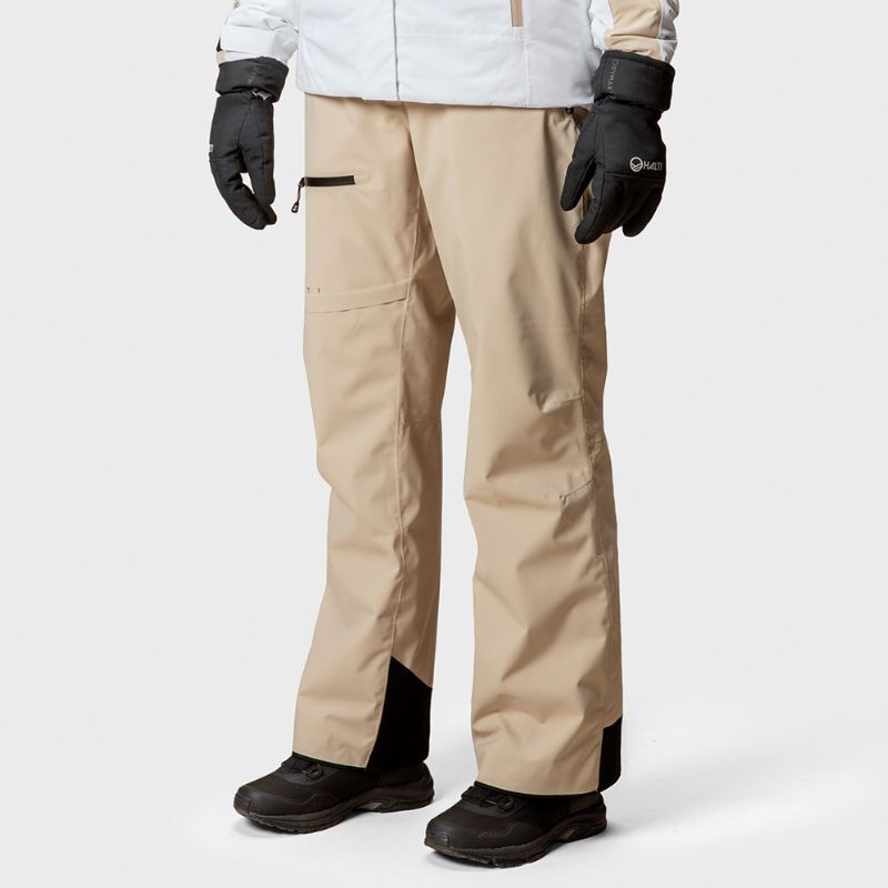 En person i Halti Carvey DrymaxX Skidbyxor Dam och en vit jacka, perfekt för skidåkning, står mot en enfärgad bakgrund.