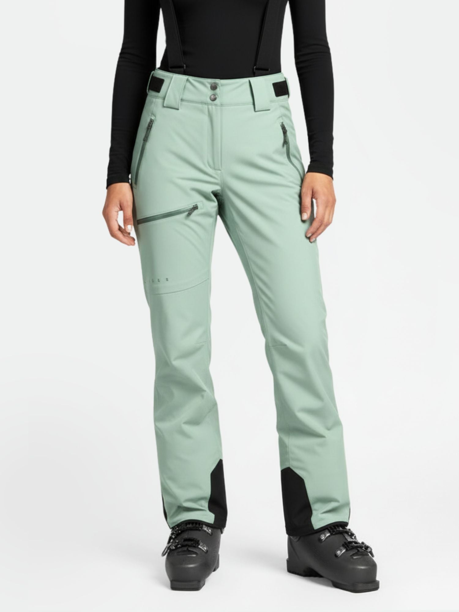 En person bär Halti Carvey DrymaxX skidbyxor dam, en svart långärmad topp och svarta skidpjäxor vända framåt.