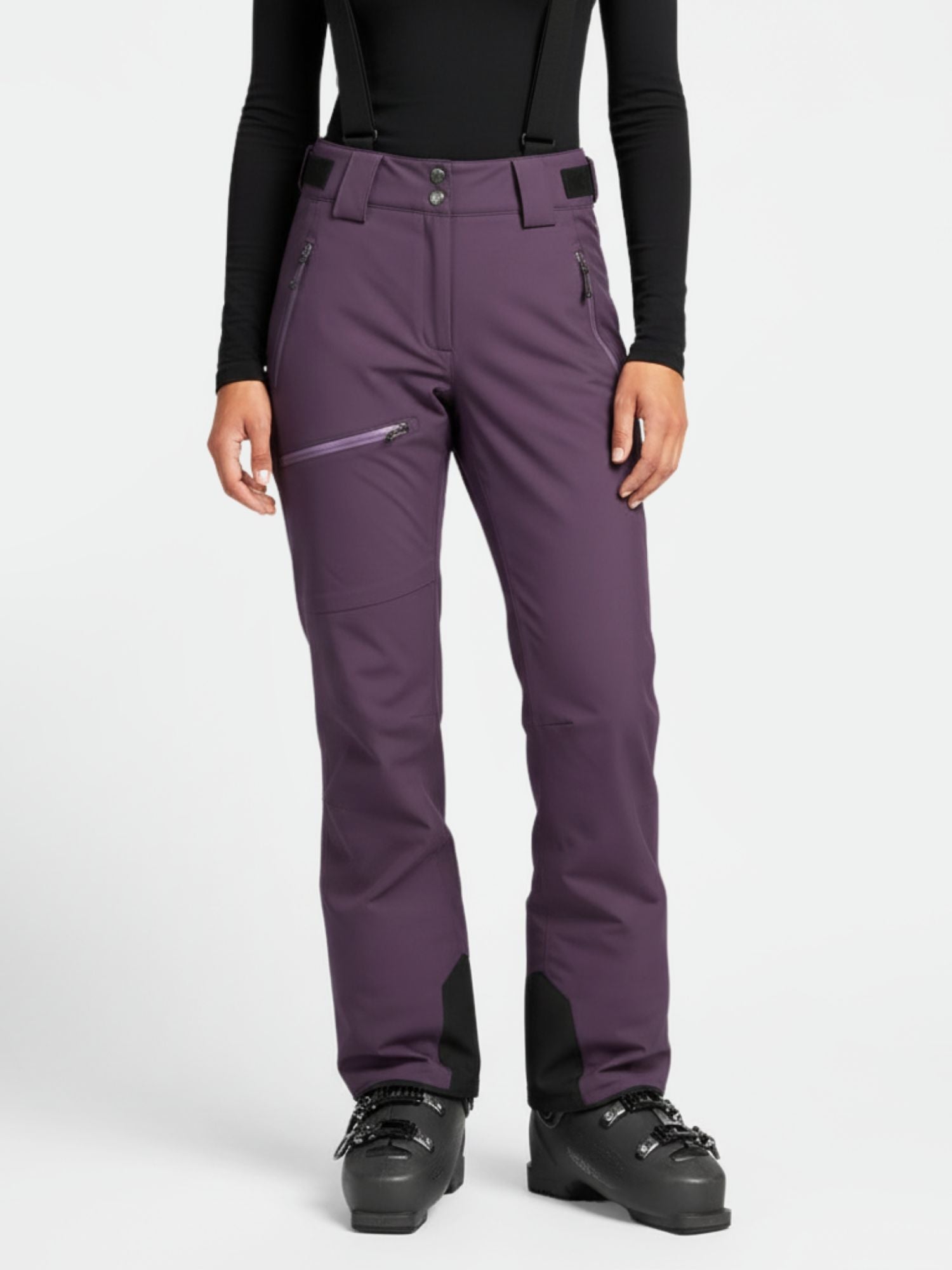 En person klädd i Halti Carvey DrymaxX Skidbyxor Dam, en svart långärmad topp och svarta pjäxor mot en vit bakgrund.