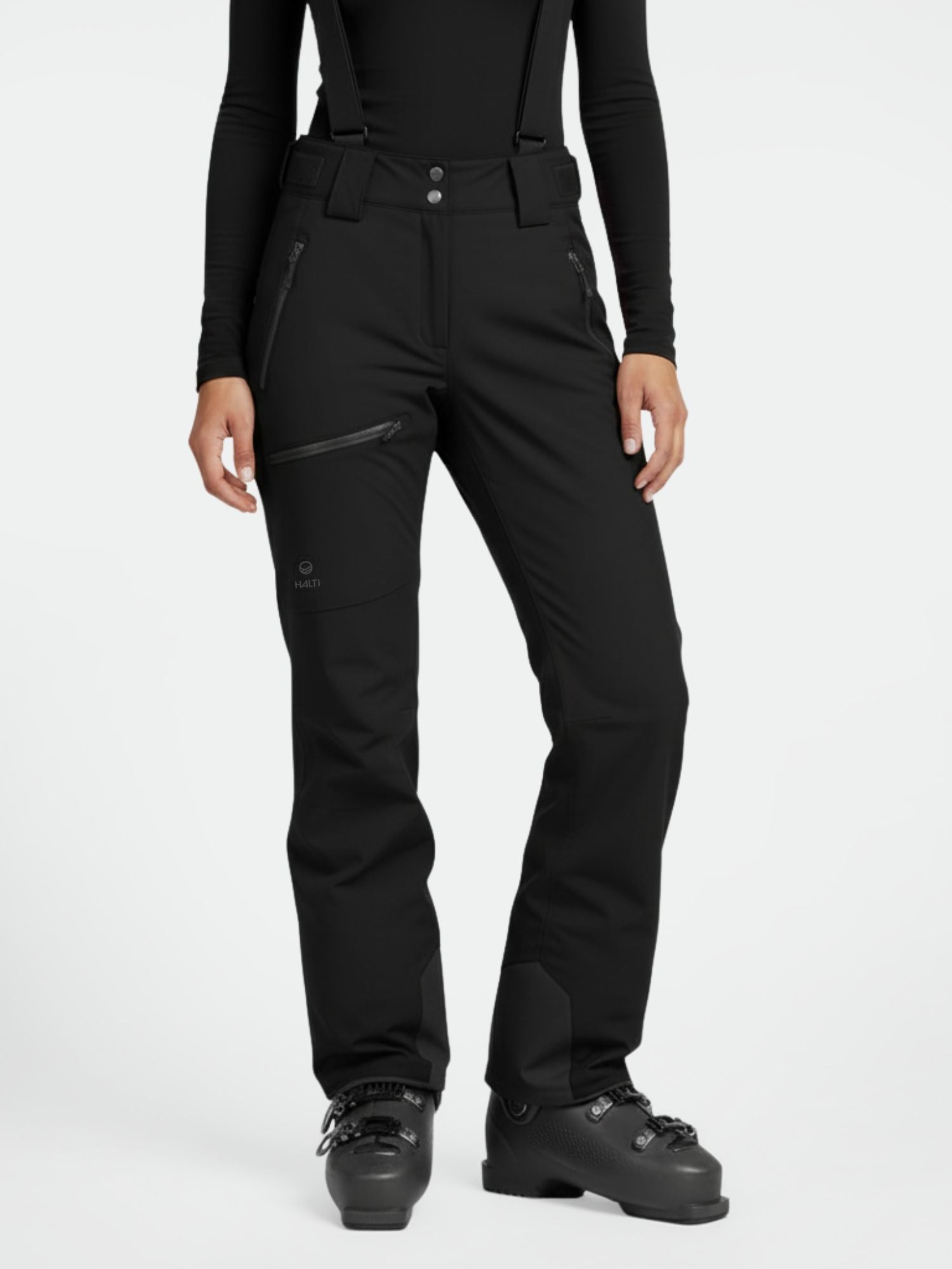 En person står upprätt i Halti Carvey DrymaxX skidbyxor dam, svart topp och boots.