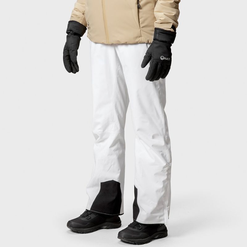Person som bär Halti Trusty DrymaxX Skidbyxor Dam, en beige jacka och svarta handskar mot en vit bakgrund.