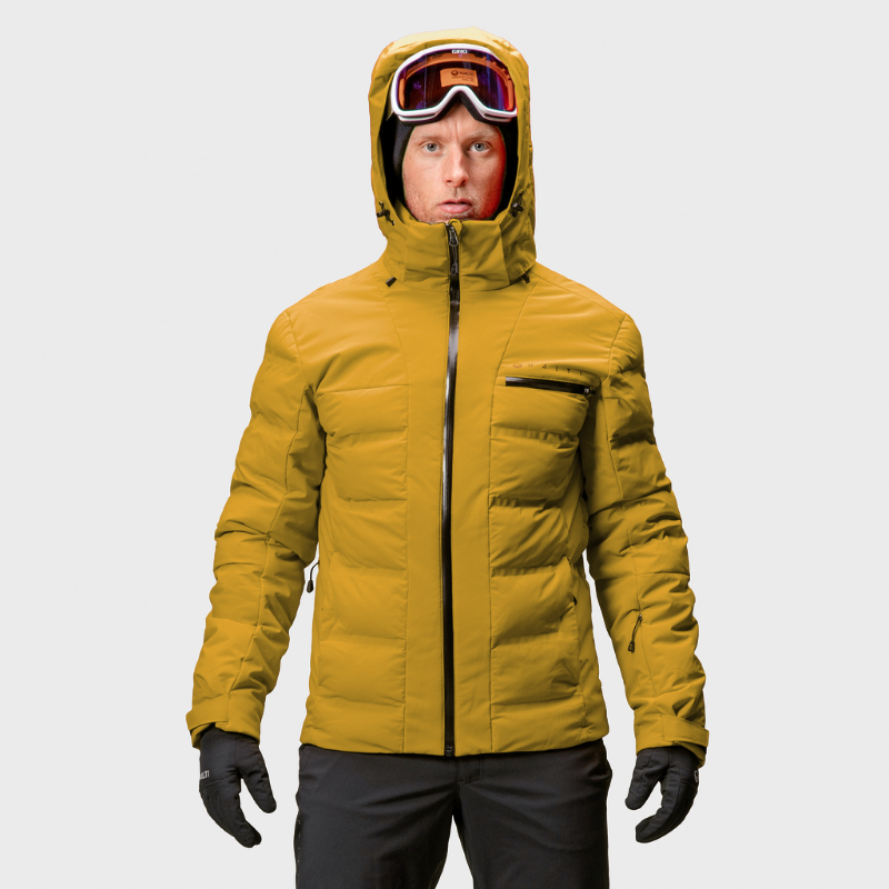 En person i en gul Halti Nordic Arcty Skijacka Herr med skidglasögon står mot en enfärgad bakgrund.