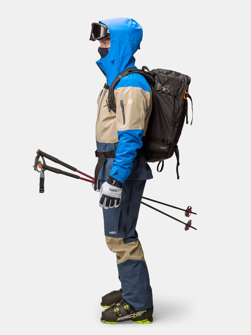 En person i blått och beige Halti Rizle 3L DX Skidjacka Unisex med Primaloft Thermo, stående vid sidan om.