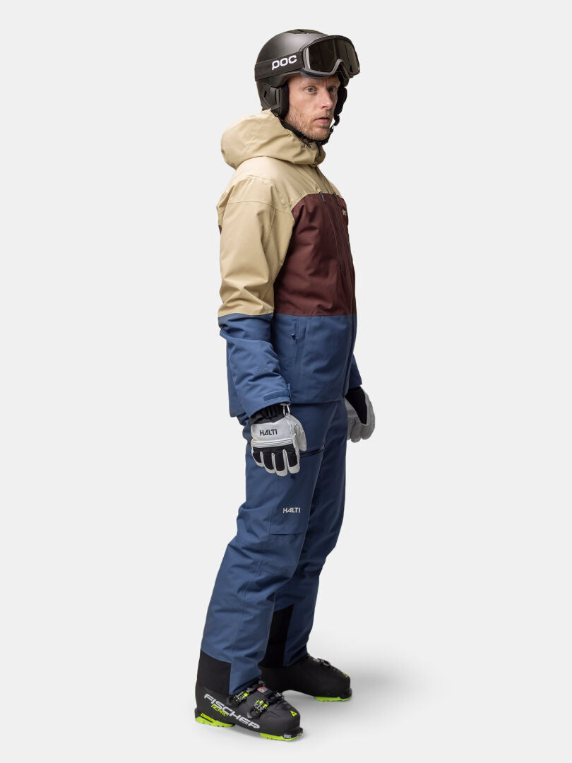 En man med hjälm, skyddsglasögon, handskar och en Halti Melvik DX Skidjacka Herr står i sidled och tittar framåt.