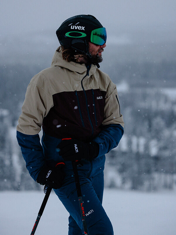 En person i en Halti Melvik DX Skidjacka Herr håller i skidstavarna utomhus en snöig dag, redo för vinteraktiviteter.