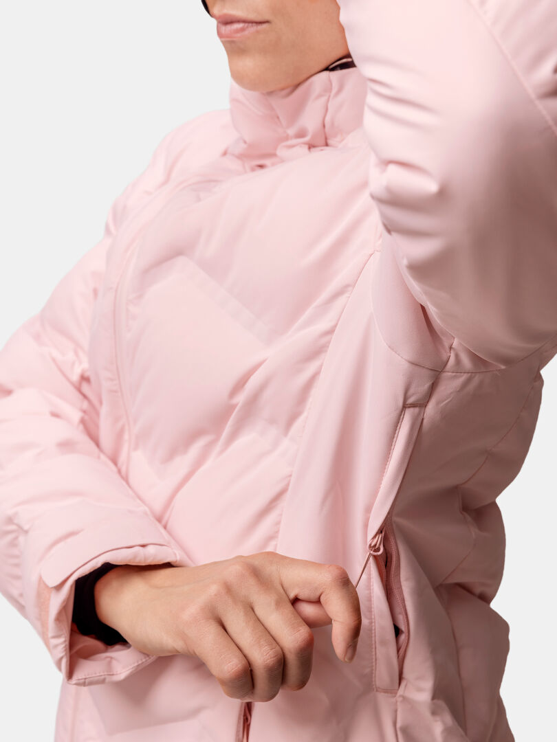 En person i en ljusrosa Halti Nordic Arcty II Skidjacka Dam öppnar ett blixtlås på sidan under armen.