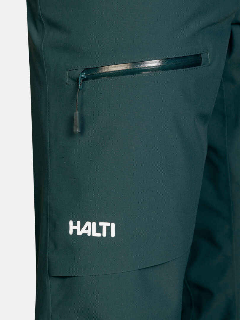 Mörkgröna Halti Carvey II DX Skidbyxor för dam med en ficka med dragkedja och en logotyp nära byxbenets nederkant.