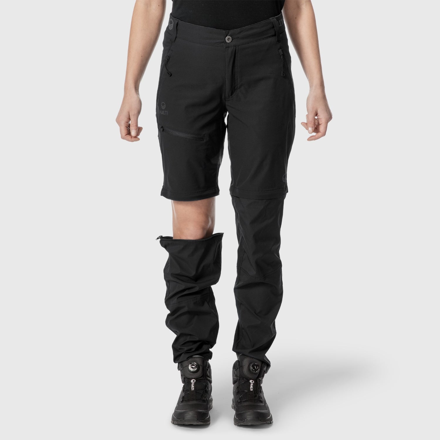 Personen bär Halti Pallas Dam X-stretch Lite Zip-off Byxor med ena benet avdraget, knät syns; grå bakgrund.