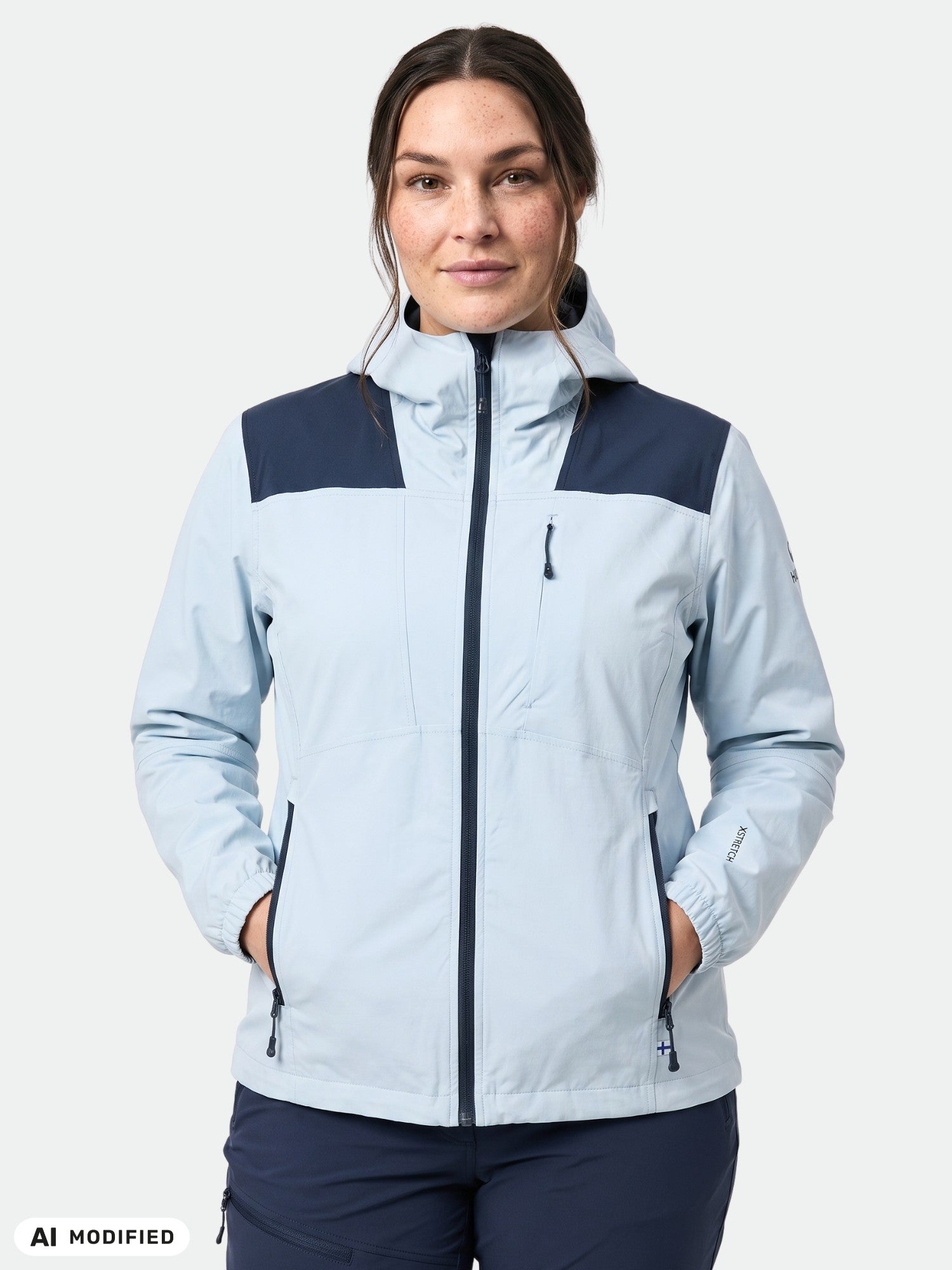 Kvinna i en Halti Pallas II Plus Dam x-stretch-jacka, ljusblå med mörkblå detaljer, med händerna i fickorna.
