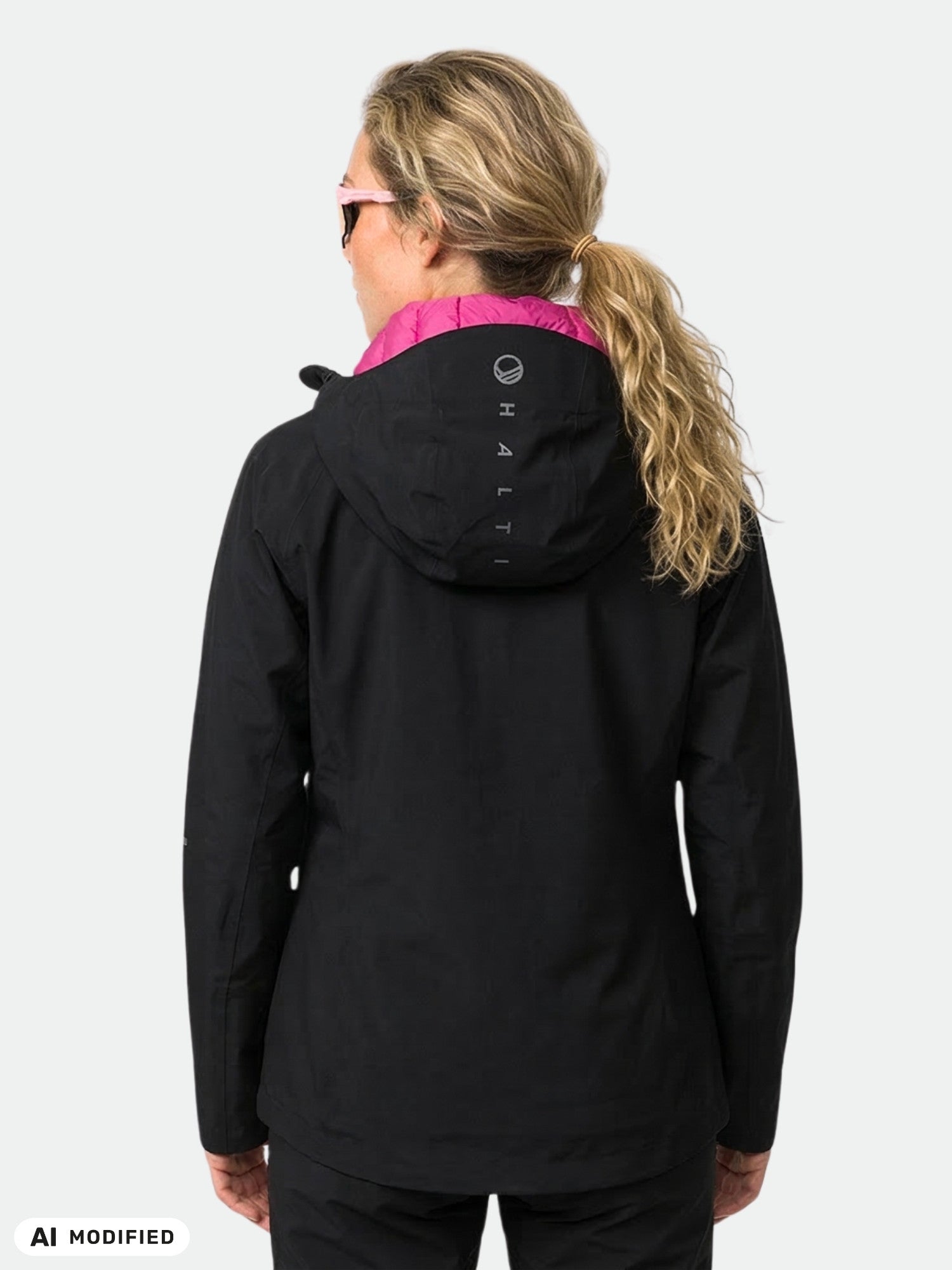 En blond kvinna bär en Halti Kaarna Dam DrymaxX 3L Skaljacka med rosa foder i huvan, sedd bakifrån mot en enfärgad bakgrund.