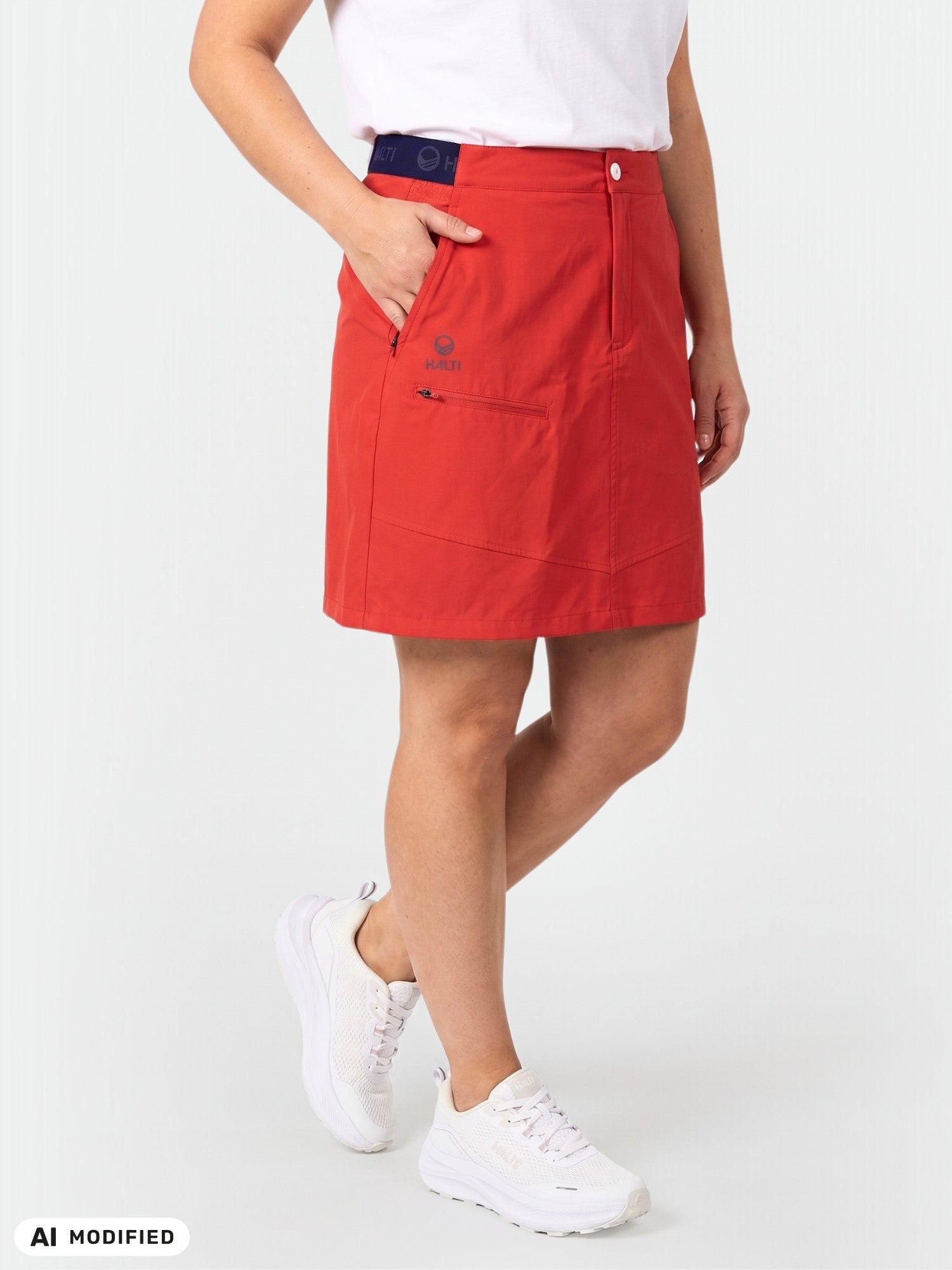 En person klädd i en Halti Pallas Dam Lite X-stretch-kjol med inbyggda shorts och vita sneakers framför en enfärgad ljus bakgrund.