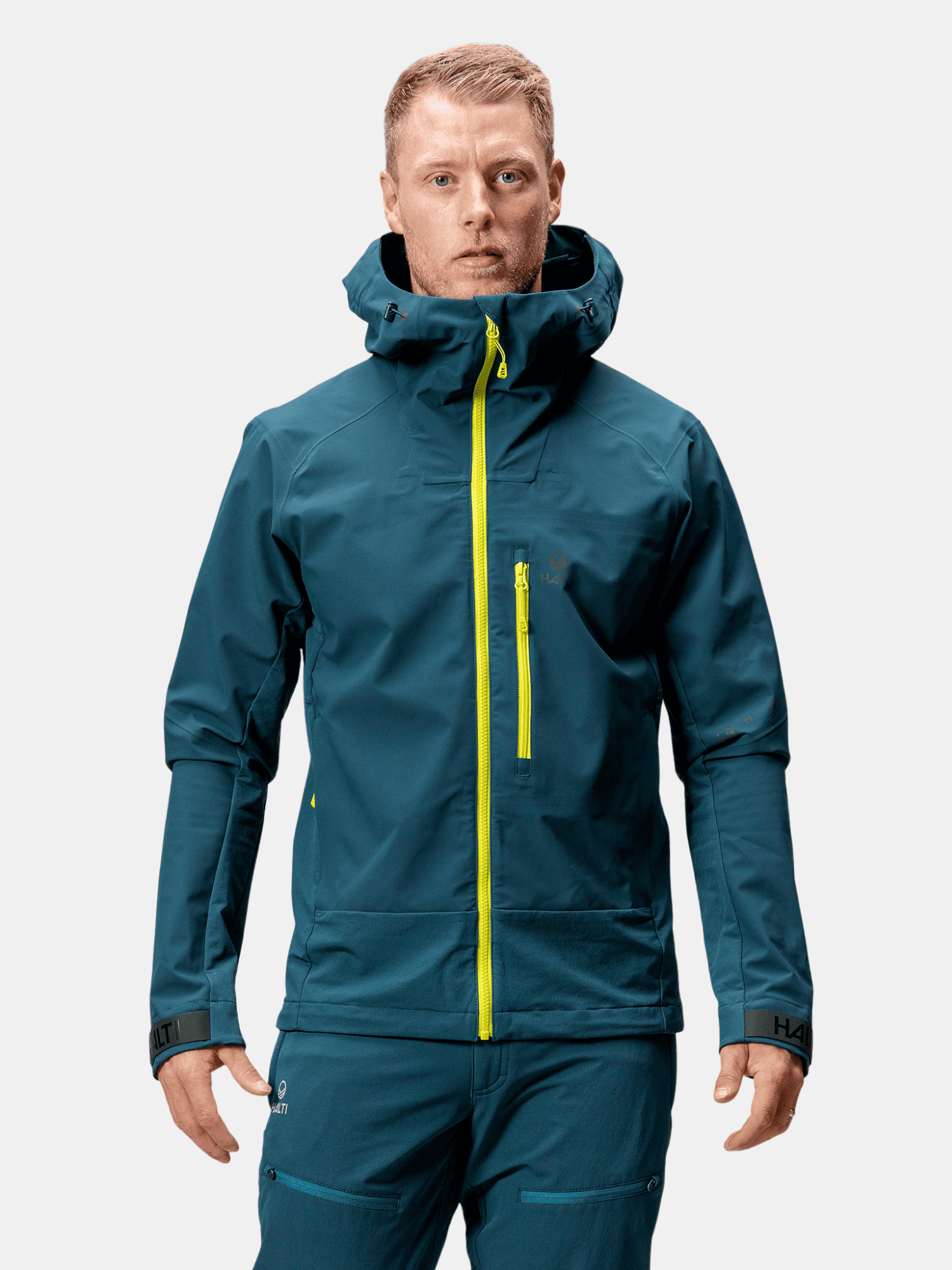 En man bär Halti Pallas III Herr Warm Hybrid Jacka, perfekt för vandring, mot en vit bakgrund.