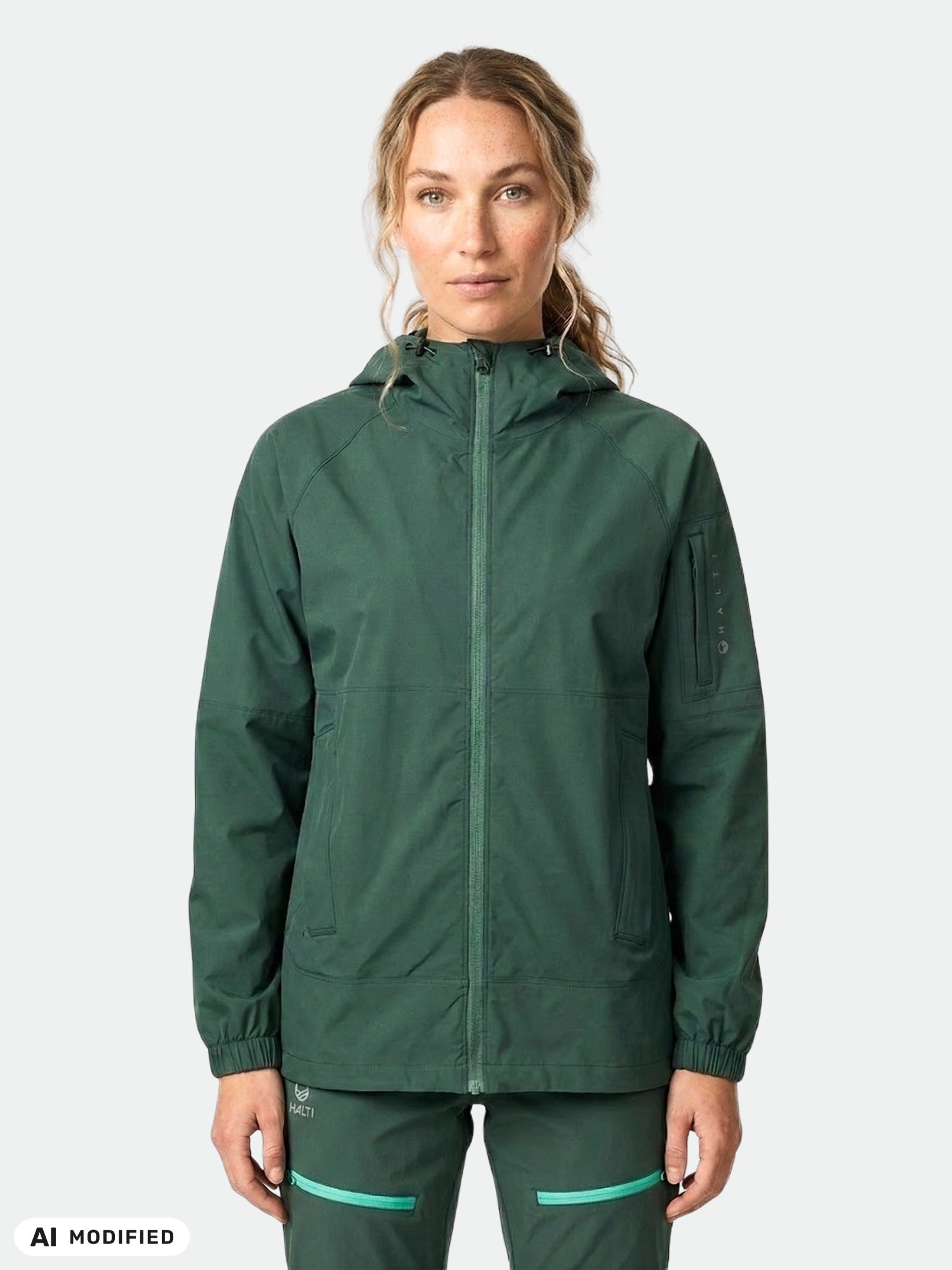 En kvinna bär en Halti Pallas Jogger Lite Jacka Dam och matchande byxor och står framför en enfärgad bakgrund.