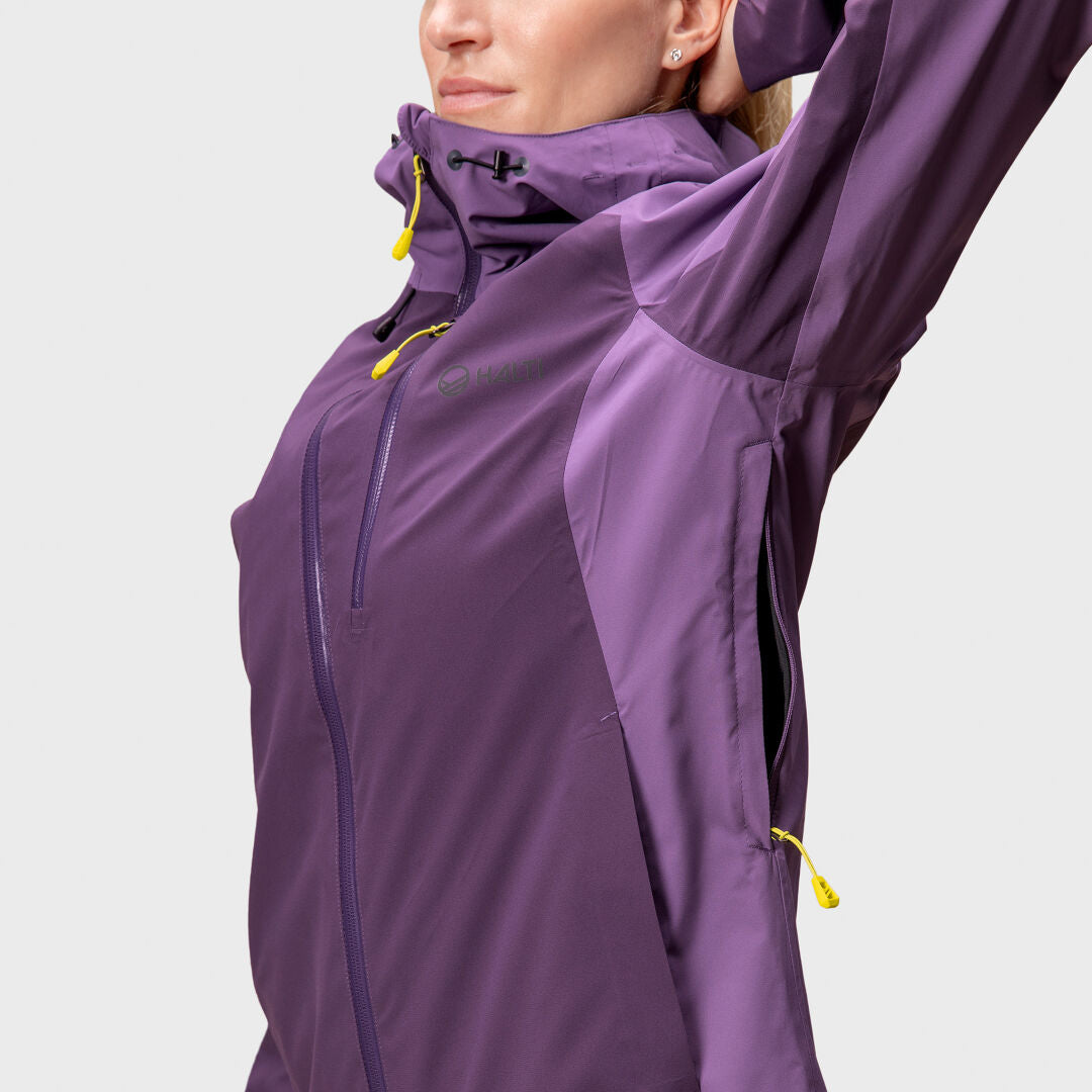 Person i en lila Halti Biegga Neve DrymaxX skaljacka med gula dragkedja, en arm upphöjd, sett från mitten av överkroppen.