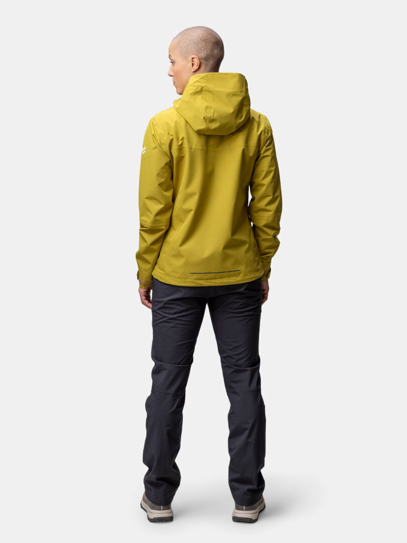 Person stående, vänd bortåt, i Halti Forter DX Skaljacka Dam och mörka byxor mot en ljus bakgrund.