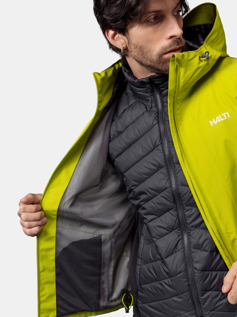 En man i en gul Halti Forter DX Skaljacka visar upp en svart quiltad innerjacka och fickfoder i nät.