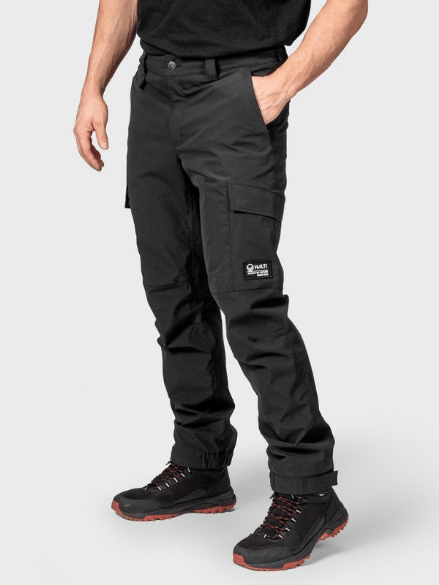 En person i svart Halti Hiker II DrymaxX Skalbyxor Herr, svart skjorta och svarta vandringskängor med röda detaljer.