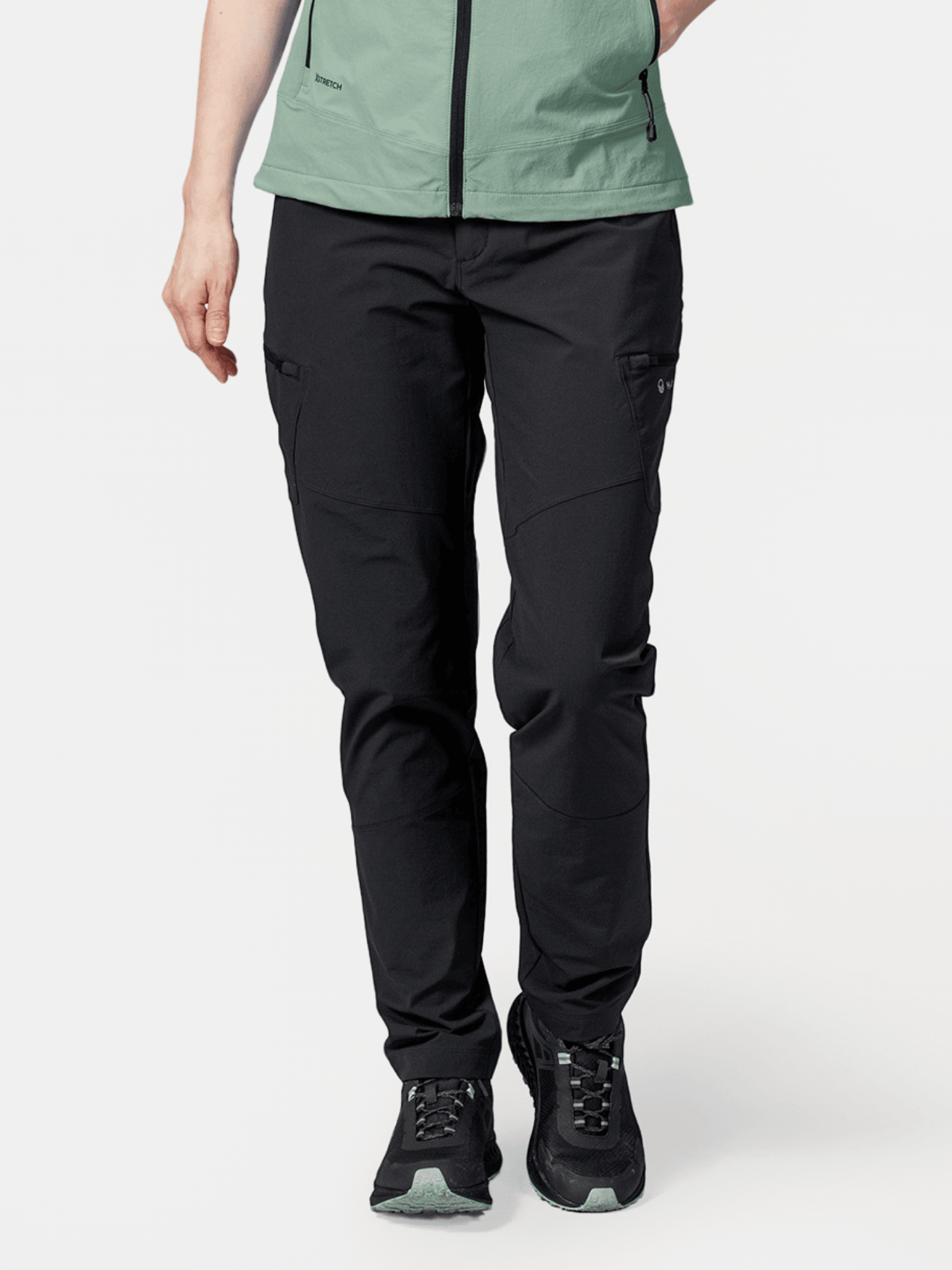 Person som bär Halti Pallas Evo X-stretch Byxor Dam, svarta sneakers med gröna sulor och en ljusgrön jacka.
