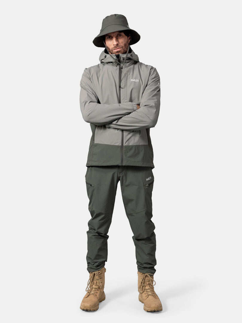 En man i Halti Pallas Evo X-stretch jacka och matchande byxor står med armarna i kors mot en vit bakgrund.