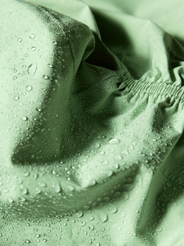 Närbild av Halti Pisarat 2,5L DX Skaljacka Dam-tyg med vattendroppar, vilket framhäver dess vattenbeständighet.