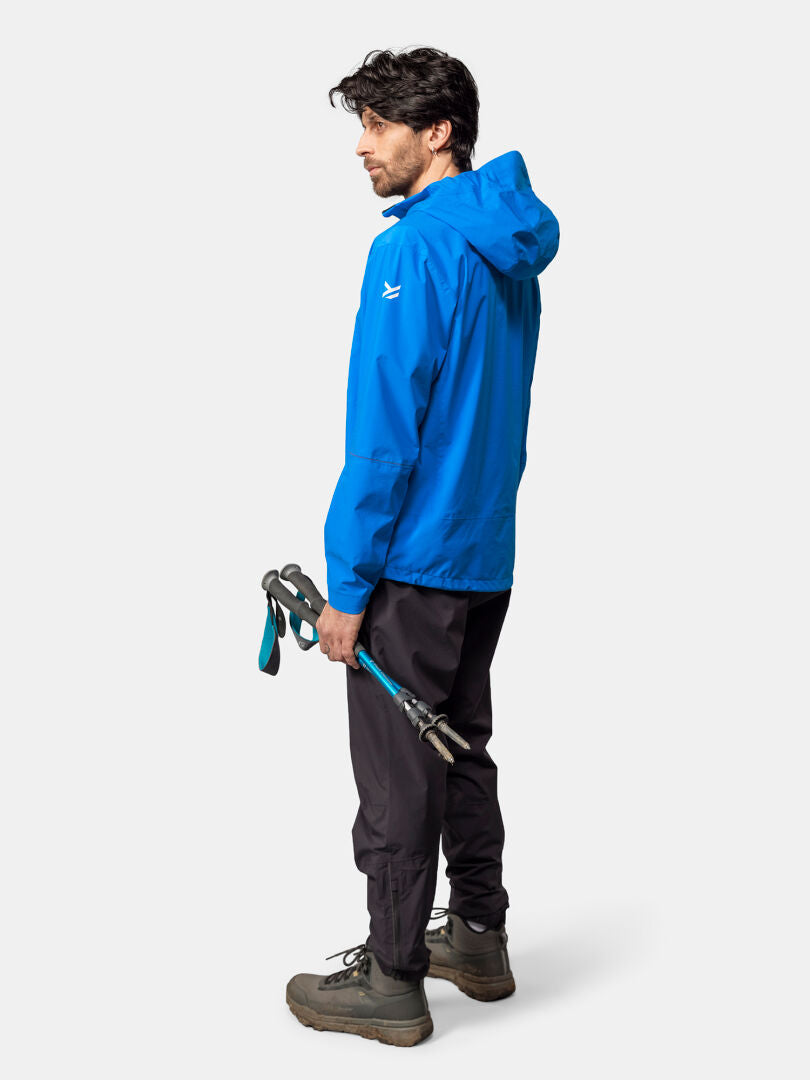 En man i en Halti Pisarat 2,5L DX Skaljacka står med vandringsstavar, vänd bort från kameran.