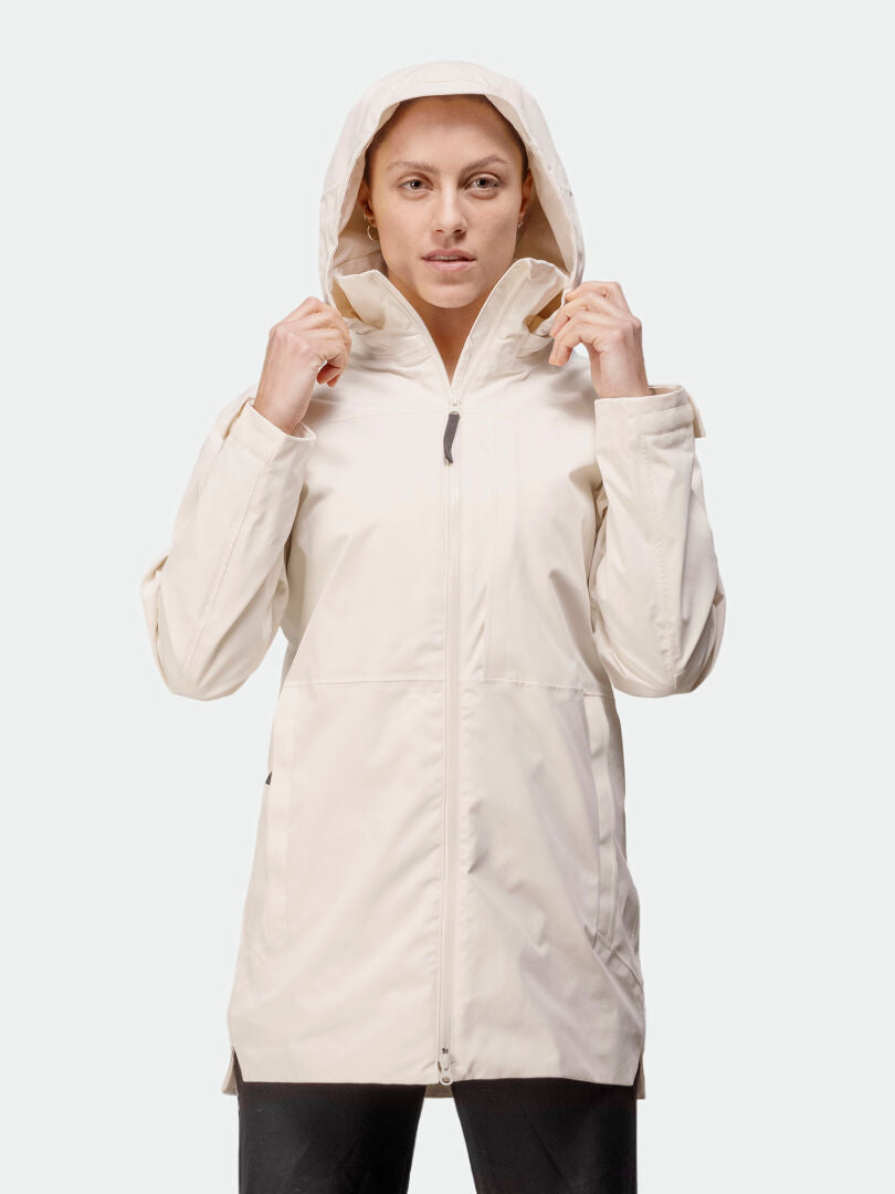 En person bär Halti Kallas DX Parka Dam i ljusbeige med huvan uppfälld, teknisk prestation, mot en vit bakgrund.
