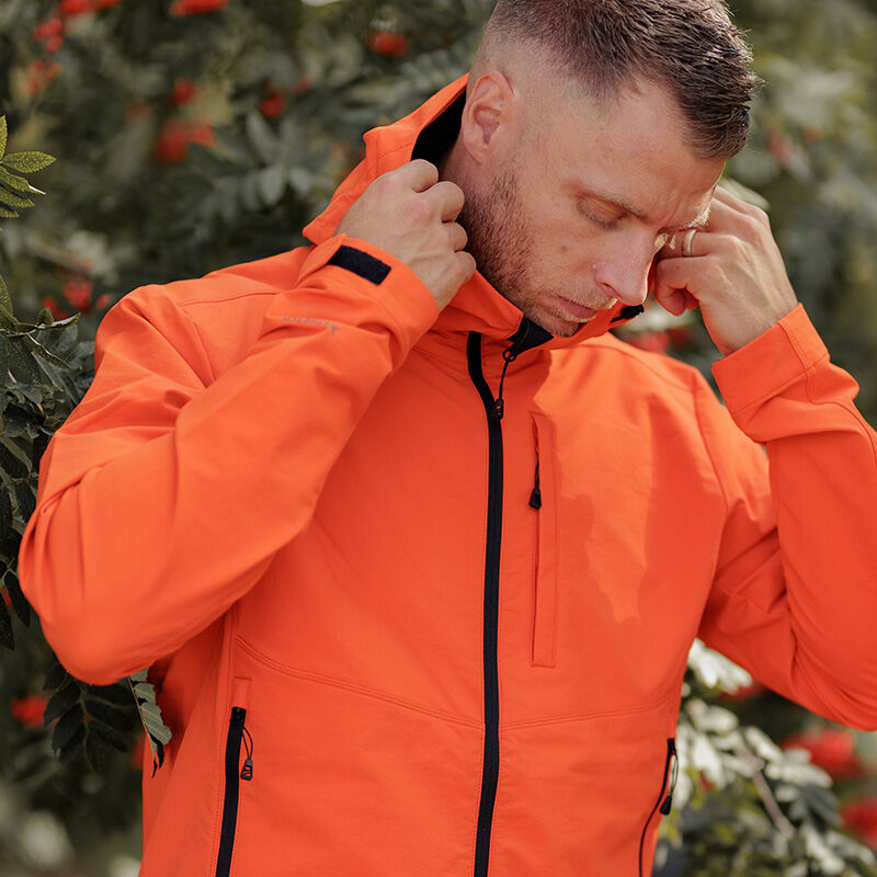 En man bär en Halti Pallas Evo Brushed X-stretch Jacka Herr nära grönt bladverk och röda bär utomhus.