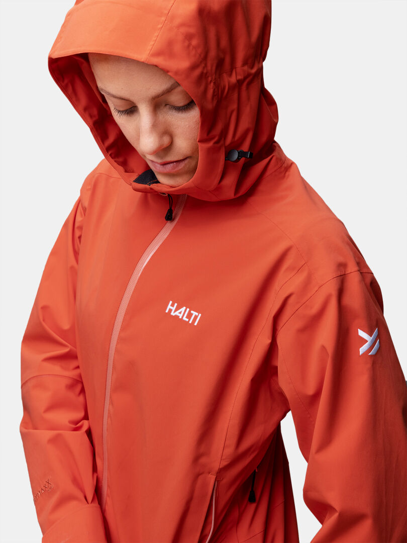 Person med orange Halti Staala DX Skaljacka Dam tittar ner mot en enfärgad bakgrund.