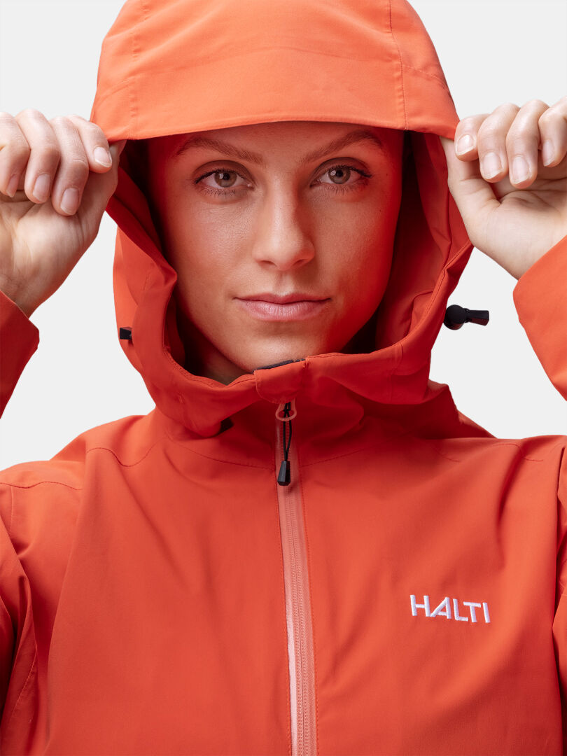 Person i orange Halti Staala DX Skaljacka Dam håller upp huven och tittar in i kameran.