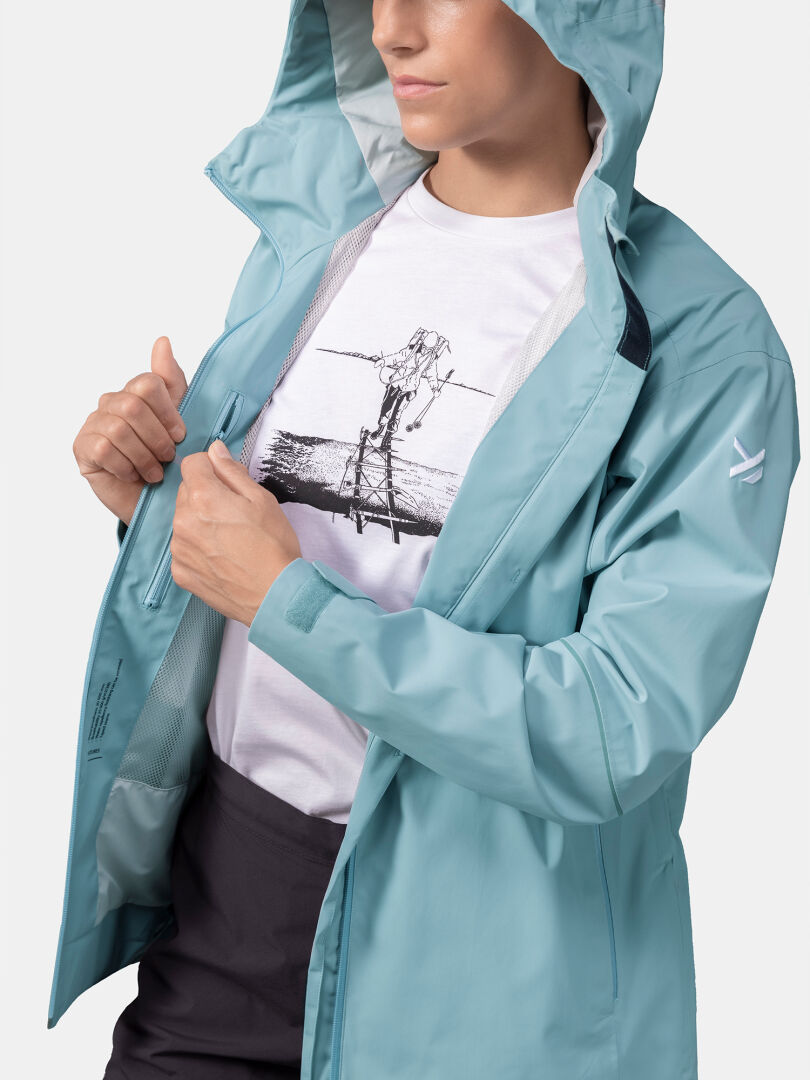 En person i en ljusblå Halti Staala DX Skaljacka Dam över en vit grafisk svartvit t-shirt.