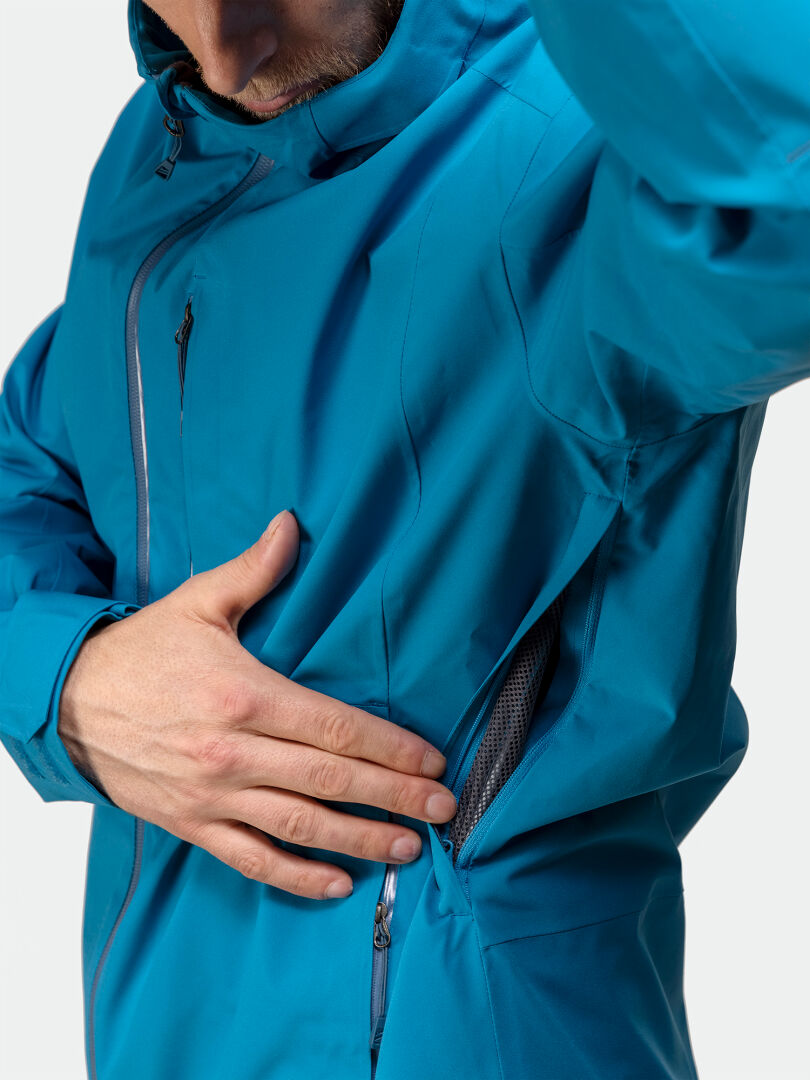 En person öppnar dragkedjan på sidan av Halti Staala DX Skaljacka Herr och visar en nätfodrad ventilationsöppning.