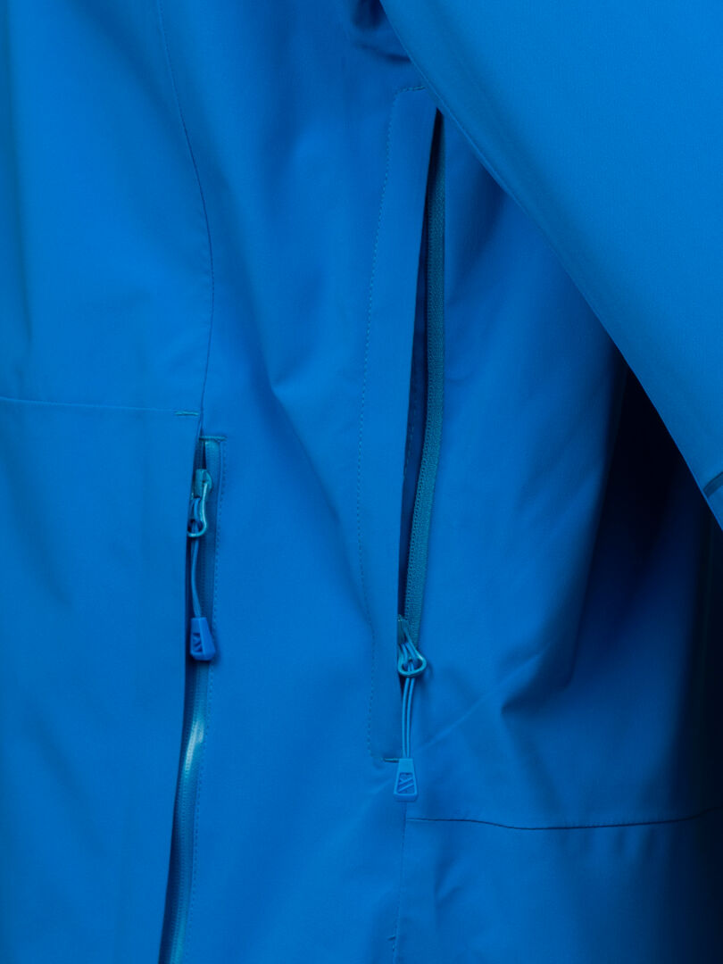 Närbild av Halti Staala DX Skaljacka Herr, med två fickor med dragkedja och blå dragkedja.