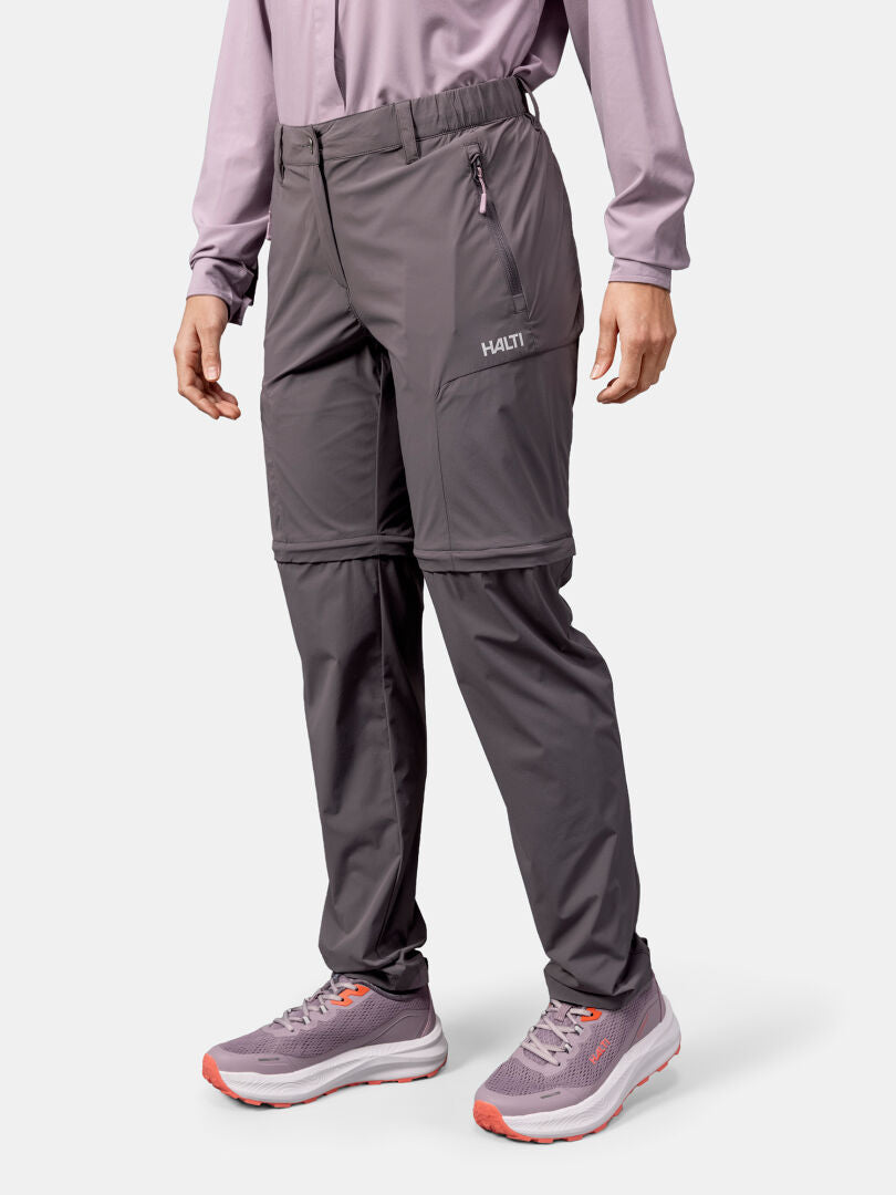 Person bär Halti Pallas Cool Stretch Zip-off Byxor Dam, långärmad tröja och sneakers med rosa detaljer.