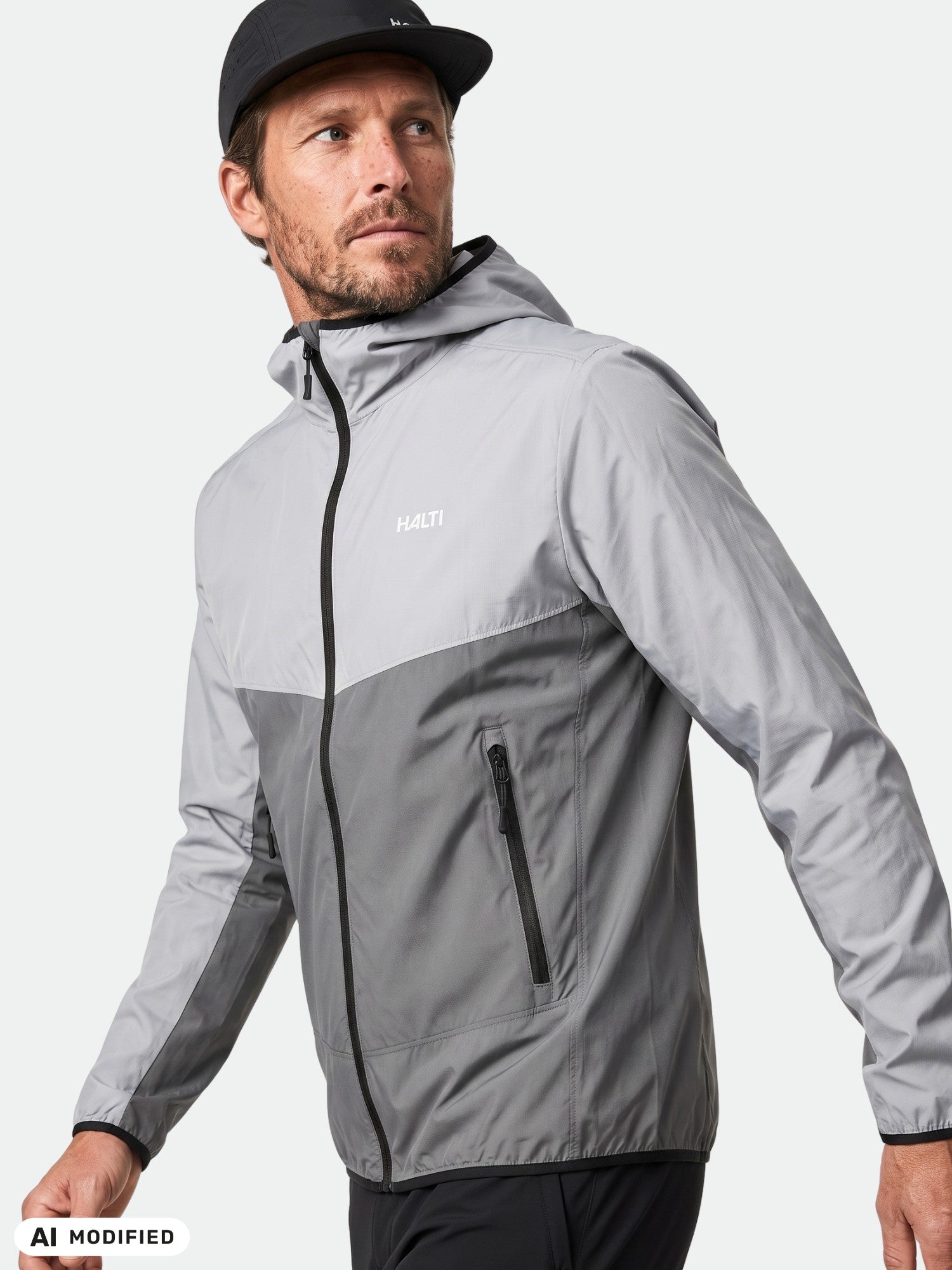 En man i en Halti Pallas Cool X-stretch-jacka och svart keps tittar åt sidan mot en ljus bakgrund.
