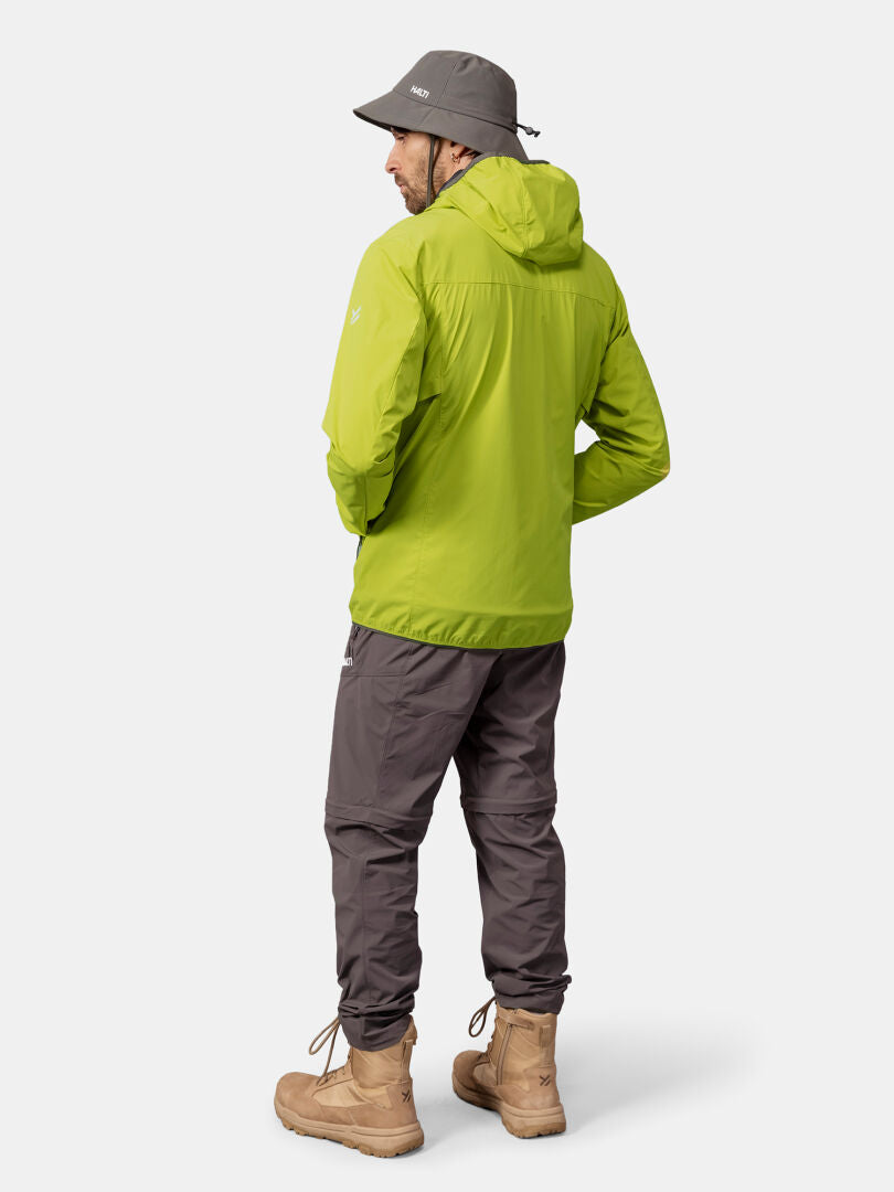 En man klädd i Halti Pallas Cool X-stretch Jacka Herr, grå byxor, bruna stövlar och en grå hinkhatt står vänd bort.