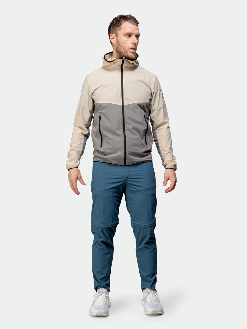 En man klädd i Halti Pallas Cool Stretch Zip-off Byxor står vänd åt vänster, tillsammans med en jacka med huva och vita sneakers.