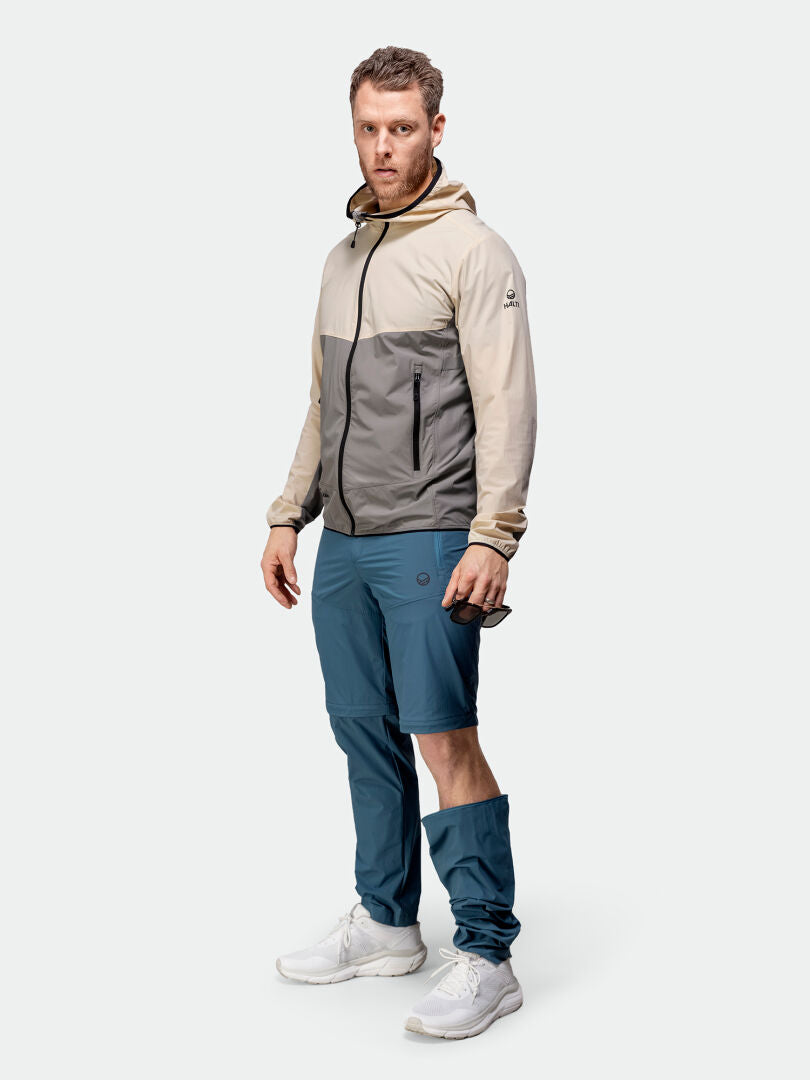 Man klädd i beige och grå jacka med huva, Halti Pallas Cool Stretch Zip-off Byxor Herr, och vita sneakers.