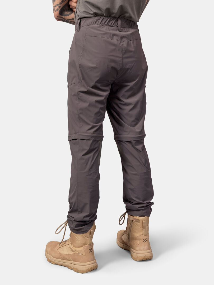 En person bär Halti Pallas Cool Stretch Zip-off Byxor Herr och solbruna stövlar, fotograferad bakifrån mot en enfärgad bakgrund.