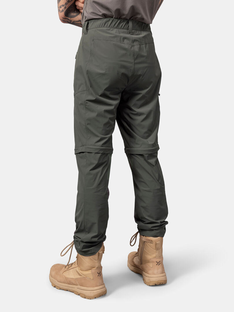 En person bär Halti Pallas Cool Stretch Zip-off Byxor Herr och solbruna stövlar, fotograferad bakifrån mot en enfärgad bakgrund.