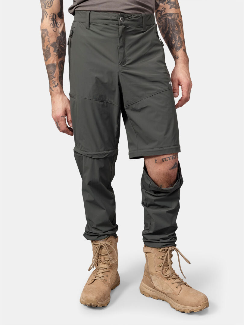 En person i Halti Pallas Cool Stretch Zip-off byxor, tan boots och tatueringar på armar och vänster ben.