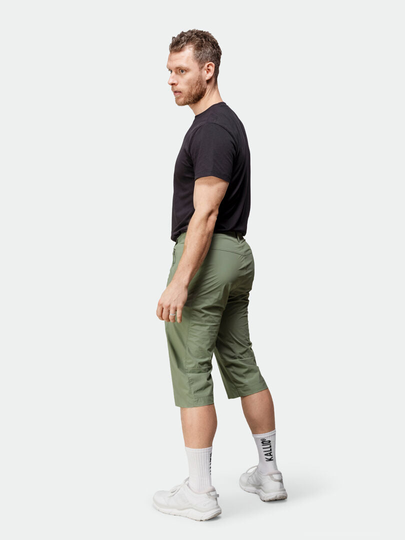 En man står ifrån sig i en svart t-shirt, Halti Pallas Cool X-stretch Capribyxor Herr, vita strumpor och sneakers.