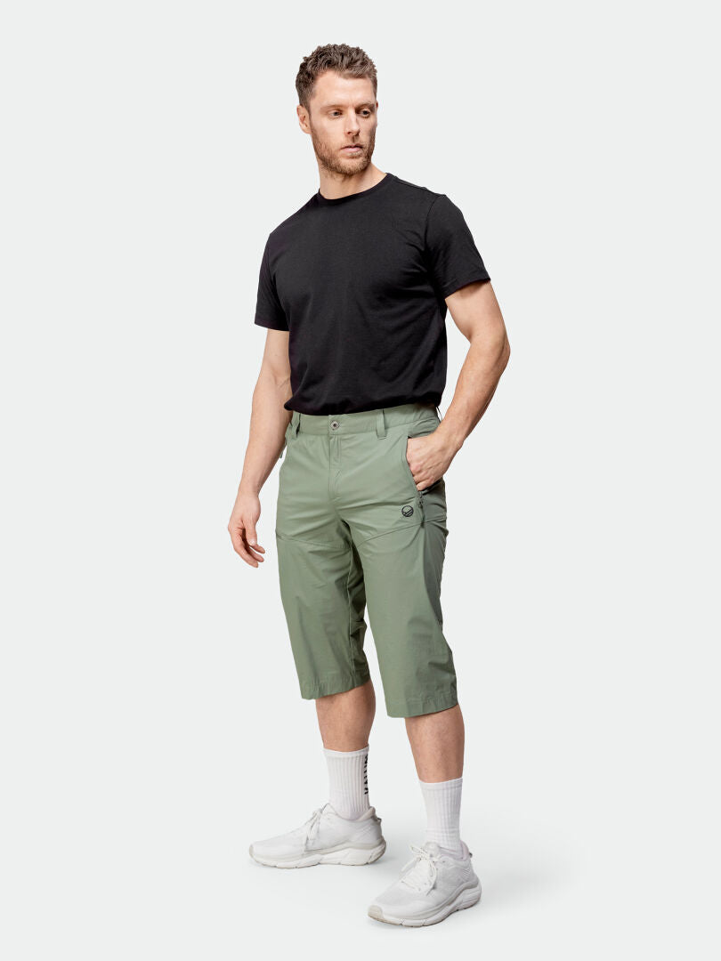 En man bär en svart t-shirt, Halti Pallas Cool X-stretch Capri-byxor Herr i ljusgrönt, vita strumpor och sneakers.